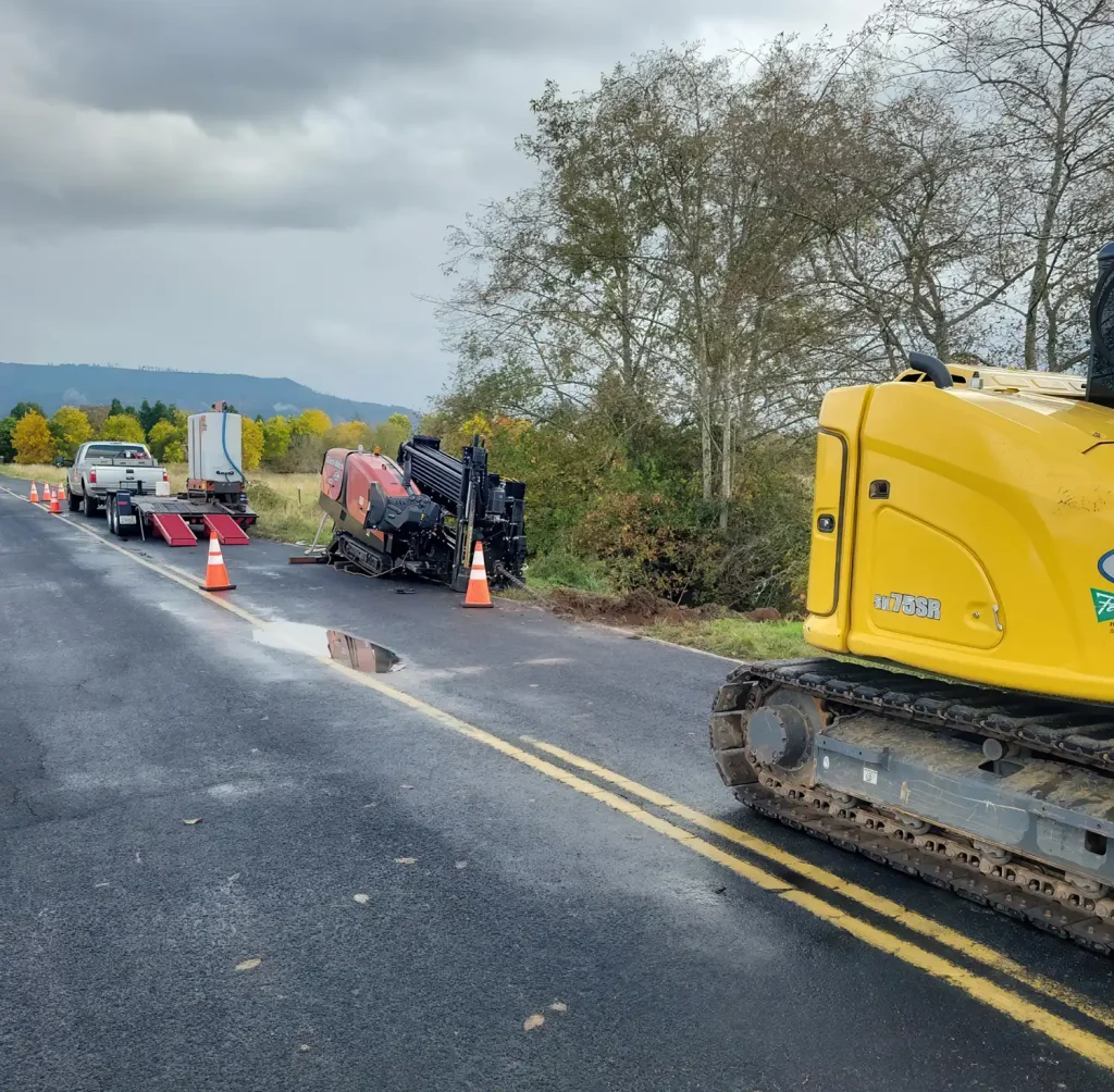 A yellow construction vehicle is parked near a flipped car on a road, with traffic cones marking the scene.