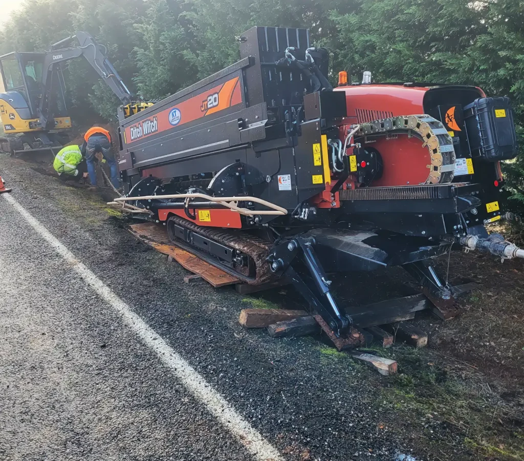Road maintenance equipment is being operated alongside a gravel road, with workers managing the machinery.