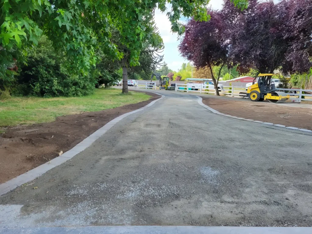 Newly paved pathway lined with trees and construction equipment in a park setting, indicating ongoing development.